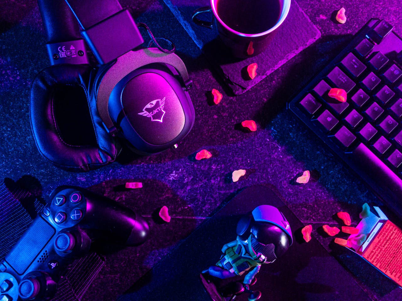 About Colorful flat lay of gaming gear including headset, controller, and keyboard under vibrant lighting.