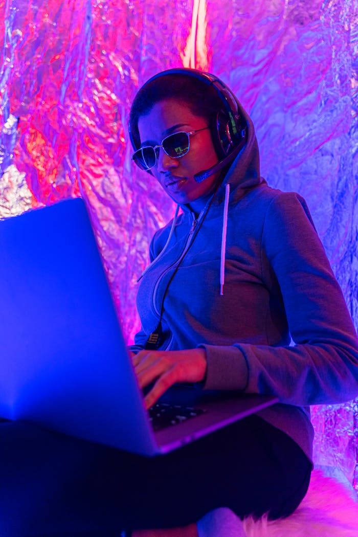 Services Woman in hoodie and headphones engaging with a laptop in a vibrant, futuristic setting.